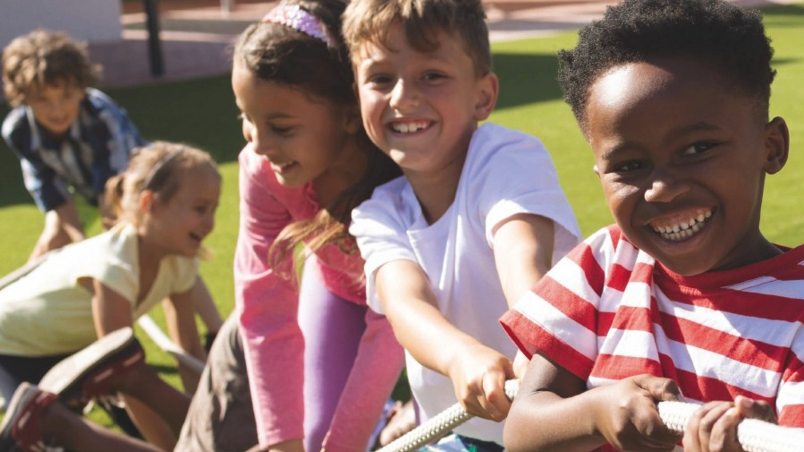 Vier fröhliche Kinder aus verschiedenen Kulturen stehen zusammen und ziehen gemeinsam an einem Seil. Ihr Lachen und die Freude in ihren Gesichtern spiegeln den Geist von Freundschaft und Zusammenarbeit wider.
