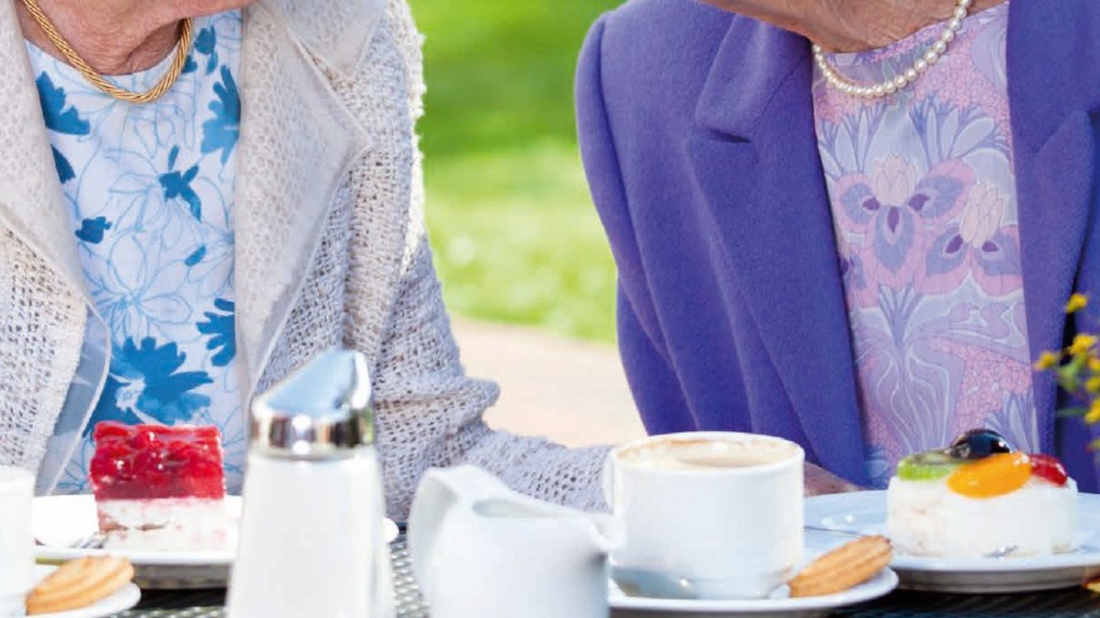 Zwei Damen unterhalten sich am Tisch und essen dabei Kuchen. Sie sind glücklich und pflegen soziale KOntakte.