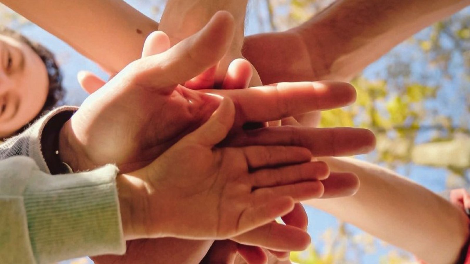 Eine Gruppe von Menschen steht eng zusammen im Kreis, ihre Hände sind verbunden und symbolisieren Gemeinschaft, Zusammenhalt und Unterstützung.